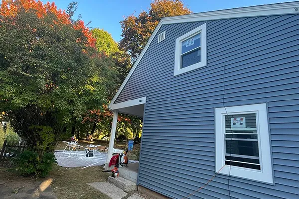 Blue vinyl siding installation on house exterior with white trim and workers