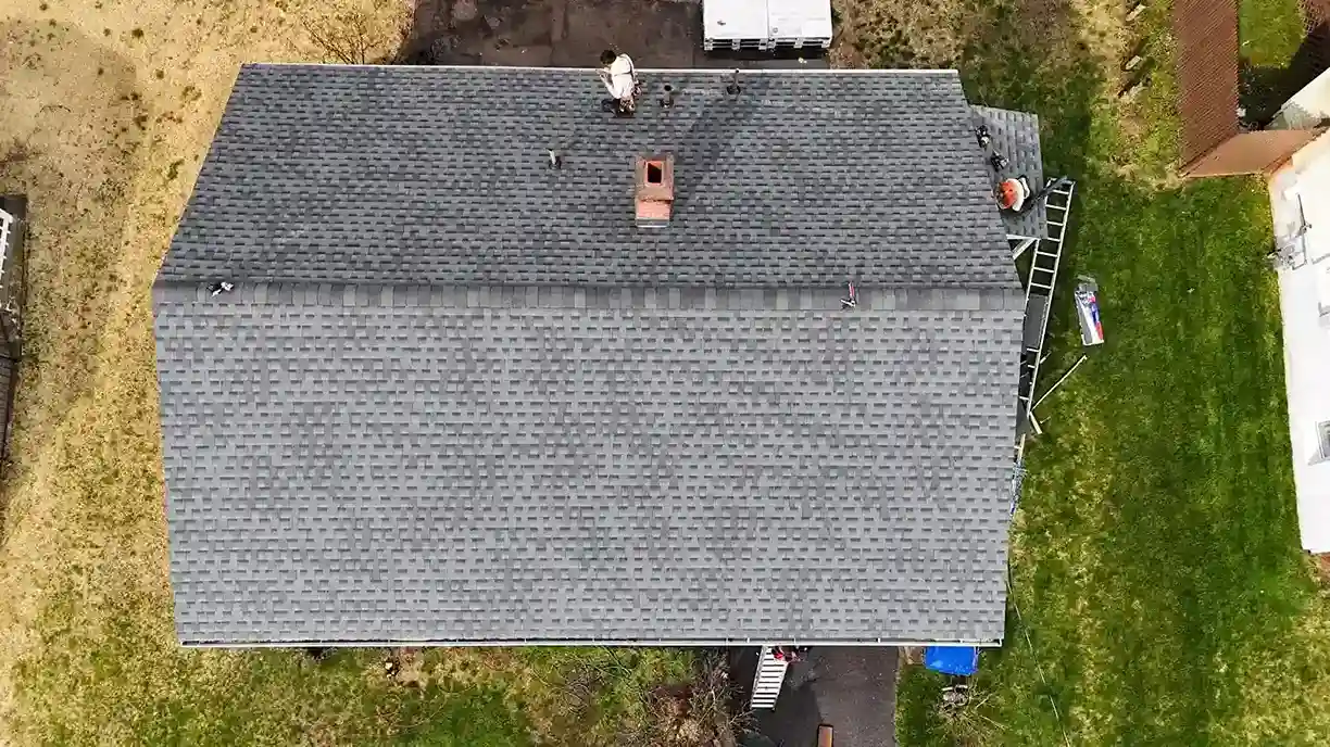 Aerial view of completed gray shingle roof with roofers and ladder in Connecticut
