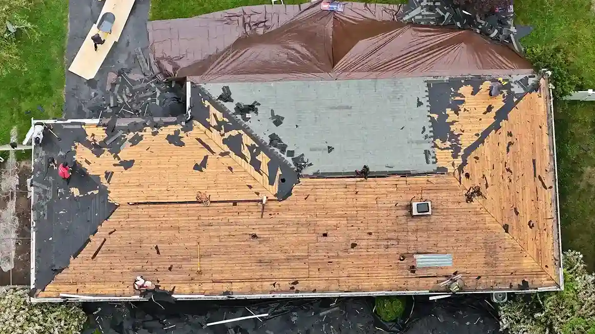 Aerial view of low-slope roof tear-off exposing plywood with tarp and workers