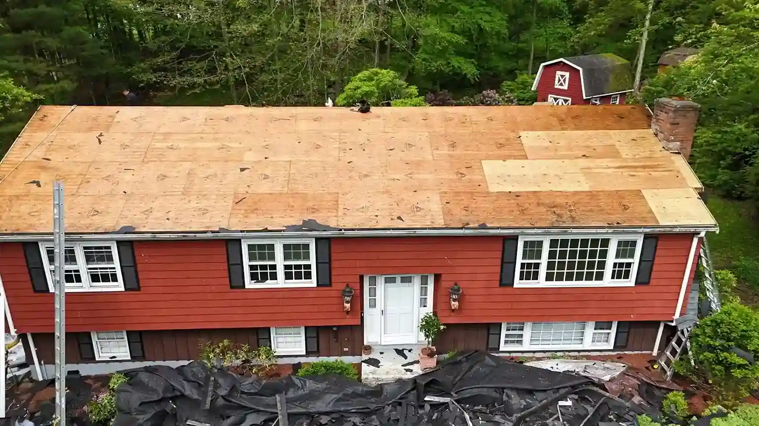 Aerial view of red house roof stripped to plywood sheathing during roof replacement