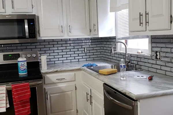 Renovated kitchen with white cabinets, blue subway tile backsplash and marble countertops