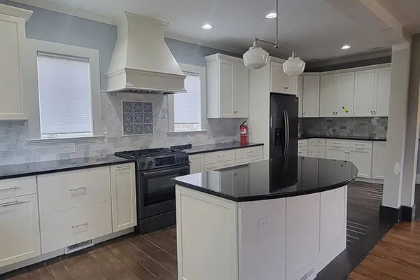 Renovated white kitchen with curved black granite island and range hood in Connecticut