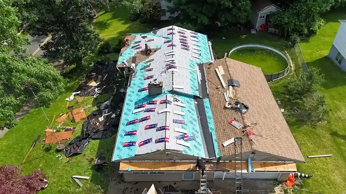 Aerial view of roof with GAF underlayment rolls and old shingles beside above-ground pool