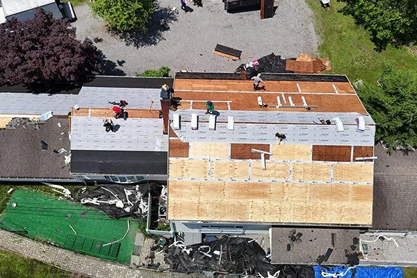 Aerial view of roof replacement in progress with workers and underlayment on house