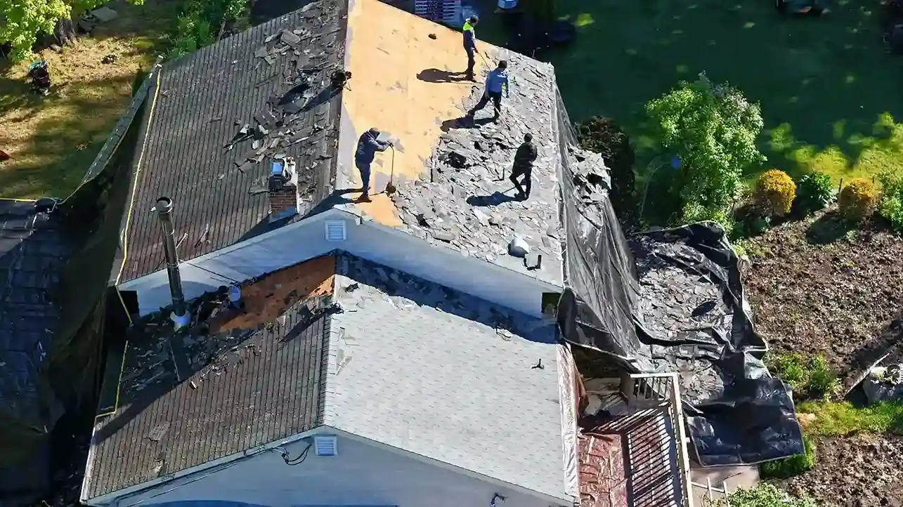 Aerial view of roof tear-off with workers and exposed plywood deck during replacement