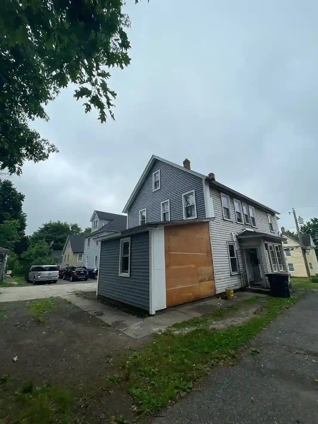 Two-story house exterior with siding removed exposing plywood sheathing during renovation